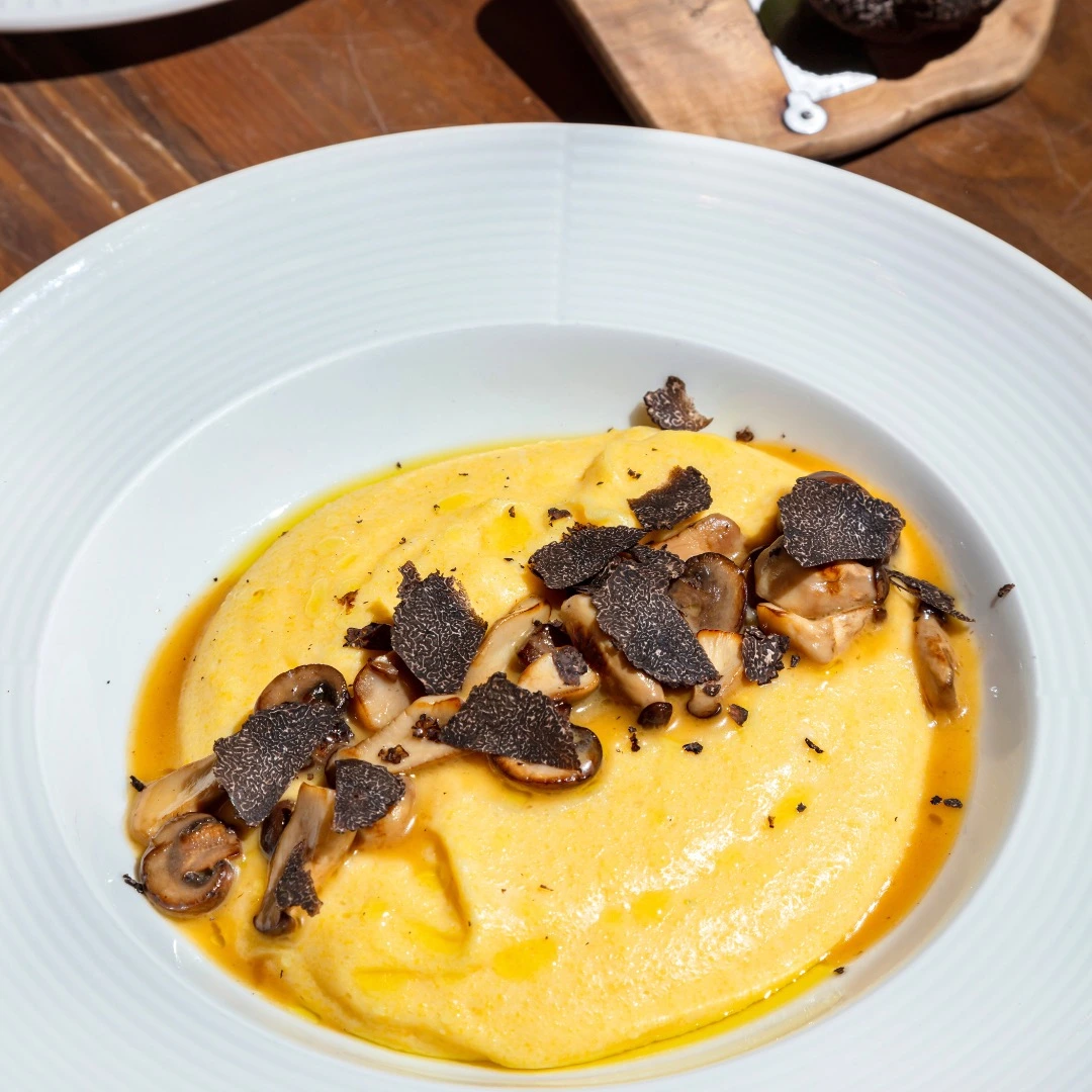 Assiette de polenta crémeuse garnie de truffe noire et de champignons, servie avec un jus savoureux.